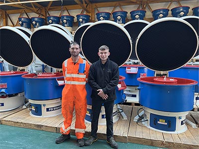 Guy Martin standing next to Adam in front of many vibratory finishing machines