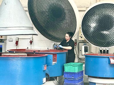 Female engineer working next to a large vibratory finishing machine in the subcon department